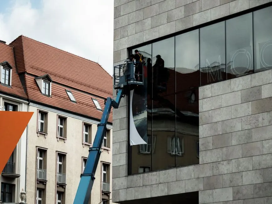 Workers on a lift install a large banner on a modern building in Wrocław, Poland.